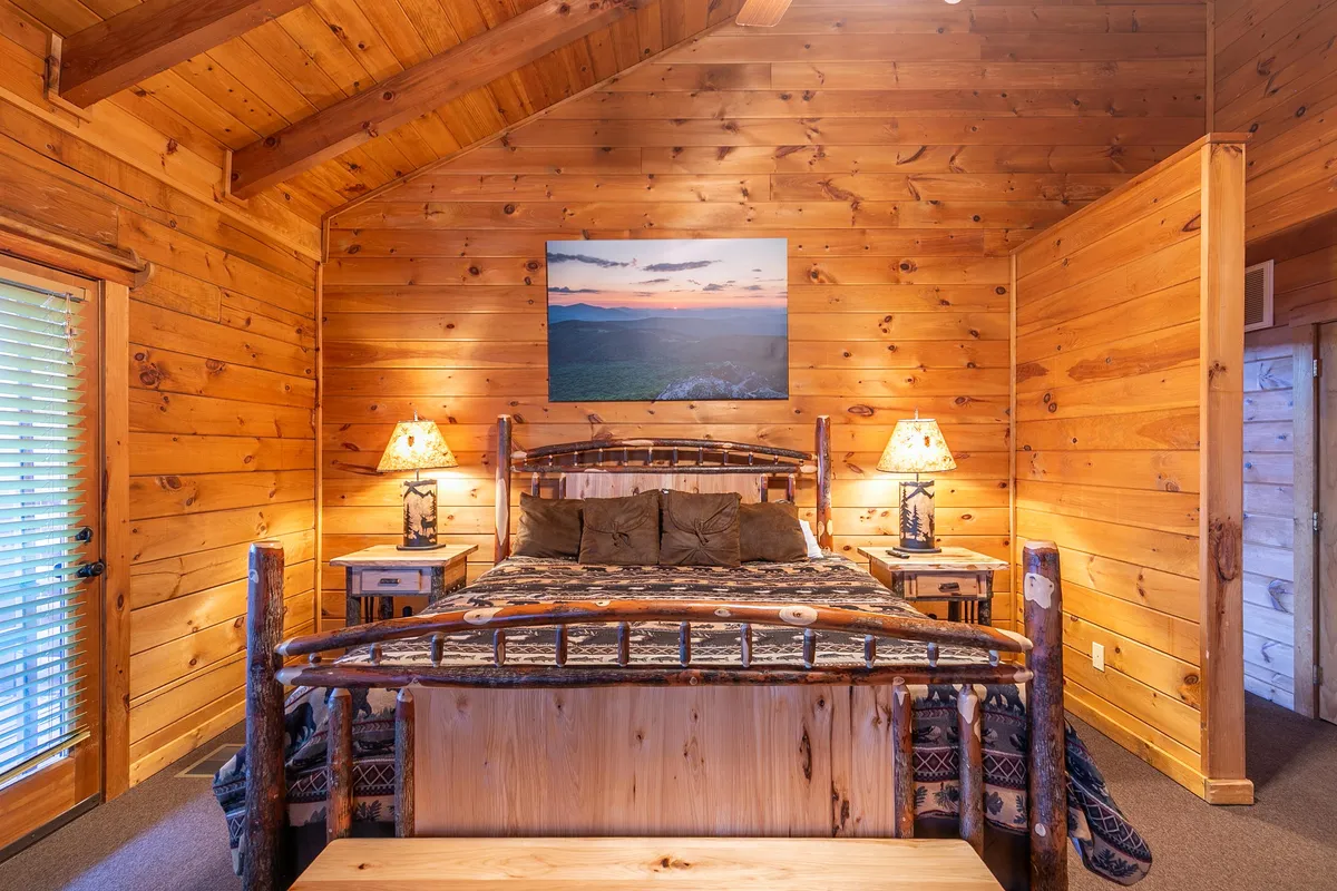 A tranquil bedroom featuring a wooden bed frame, landscape artwork above the headboard, and soft bedside lighting. The room's serene color palette and thoughtful details create a peaceful, welcoming environment ideal for unwinding after an adventurous day.