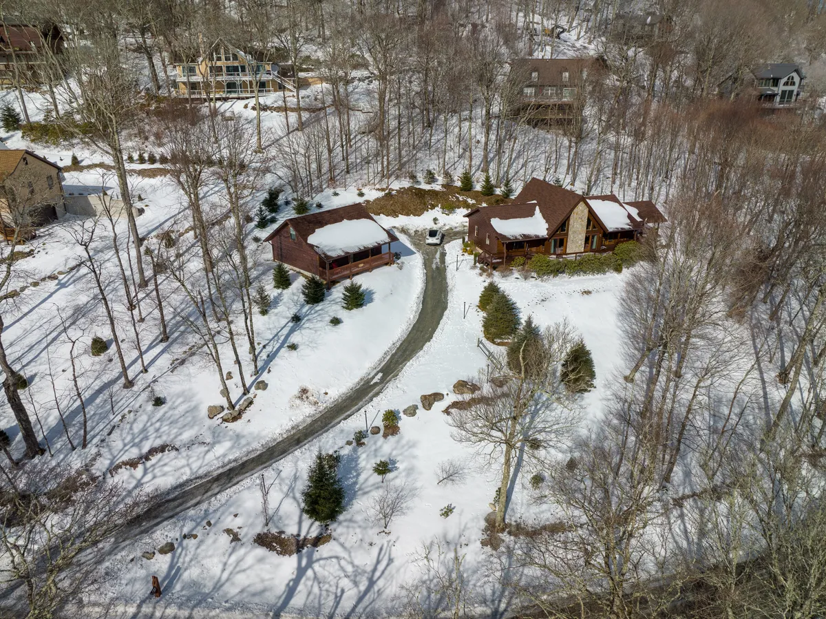 A picturesque winter scene showing a snow-covered landscape with a curved driveway leading to wooden houses. The area is surrounded by trees and landscaped gardens, evoking the ideal setting for winter sports and snowy adventures.