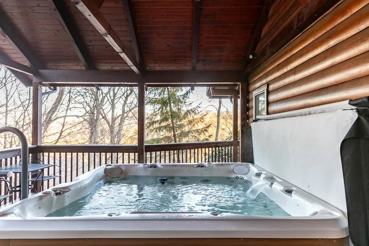 This exterior image features the inviting hot tub set on a wooden deck, surrounded by natural scenery. The tranquil setting highlights the opportunity to soak in the hot tub while enjoying mountain views and the peaceful outdoors.