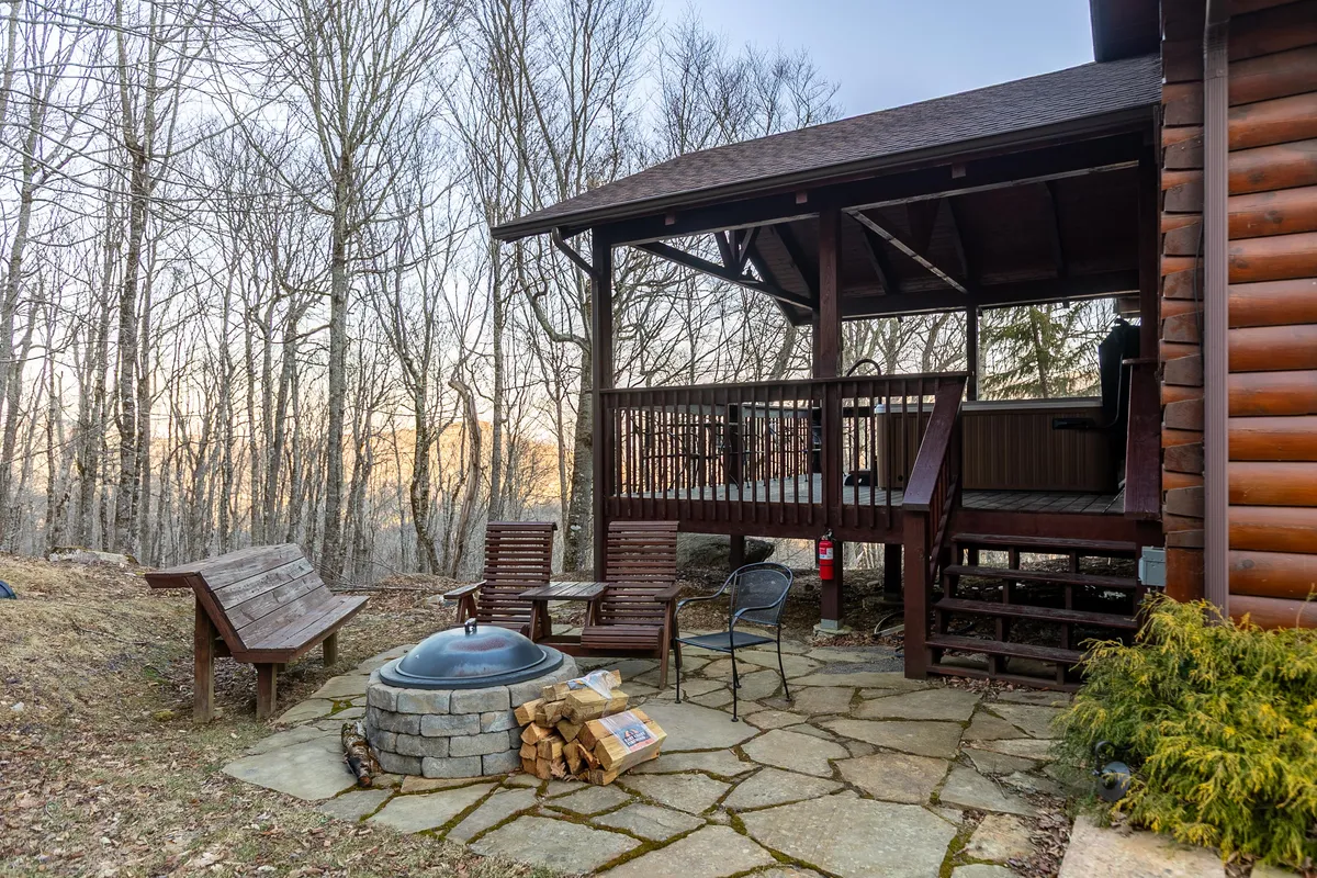 An exterior shot focusing on the firepit area, featuring wooden benches and a deck area. The setup is perfect for group gatherings, sharing stories, and enjoying the crisp mountain air under the stars.